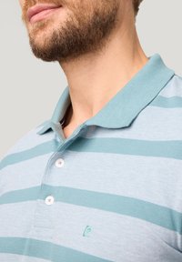 Lichtblauw poloshirt met afwisselende teal strepen, voorzien van een kraag en drie witte knopen. Klein logo op de borst. Katoenen stof.