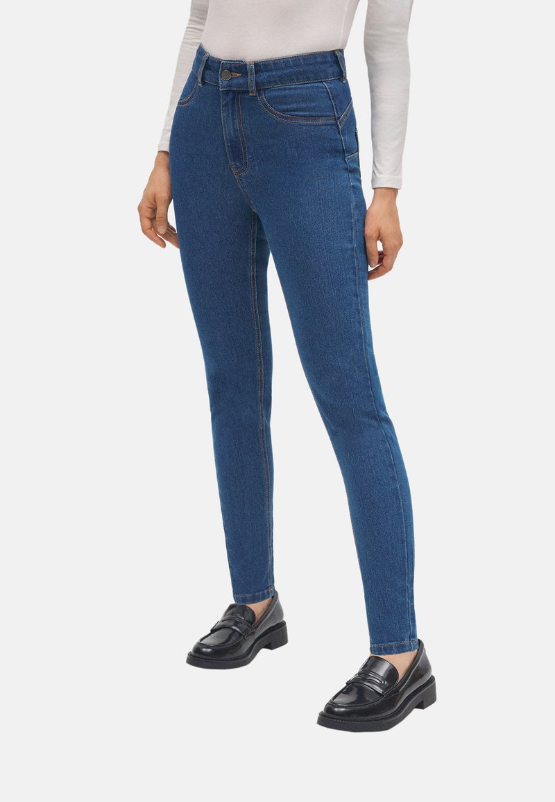 Jeans ajustados de mezclilla azul con una cintura alta, que presentan costuras naranjas en contraste y un diseño clásico de cinco bolsillos. Textura suave.