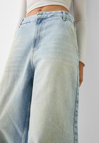 Light blue wide-leg jeans made from denim, featuring a high waist, front button closure, and subtle fading. Smooth texture and classic design.