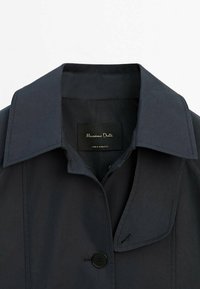 Donker marineblauwe jas met een grote kraag, knoopsluiting en zijnaadstiksels. Heeft een label "Massimo Dutti" aan de binnenkant van de kraag.