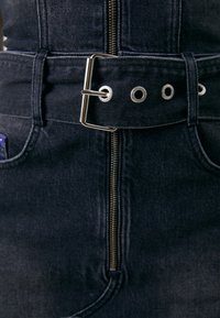 Temno jeans obleka z zadrgo spredaj, ki ima širok pas z kovinsko sponko in obroči. Gladka tekstura in strukturiran dizajn.