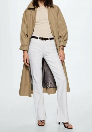 Tan trench coat over a beige top, paired with white flared jeans and black strappy sandals. Notable details include a brown belt and coat lining.