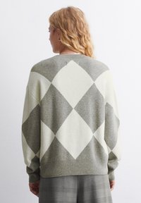 Graugemusterter und cremefarbener Argyle-Strickpullover mit lockerer Passform, Rundhalsausschnitt und gerippten Bündchen, von hinten betrachtet.