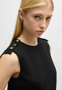 Schwarzes ärmelloses Oberteil mit strukturiertem Schulterdesign und silbernen Knöpfen. Glattes, mattes Material mit klaren Linien und taillierter Form.