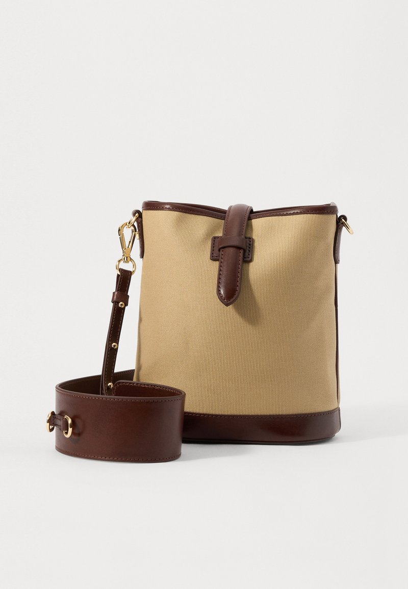 Canvas-Einkaufstasche in Beige mit schokoladenbraunen Lederakzenten. Verfügt über einen oberen Klappverschluss, einen verstellbaren Trageriemen und goldfarbene Hardware.