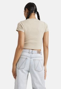 Beige short-sleeve crop top with a fitted design, paired with high-waisted light blue jeans featuring diagonal pocket stitching and a leather tag.