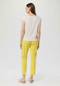 White short-sleeve top with lace trim paired with yellow tapered pants. Model wears beige slingback shoes, viewed from the back.
