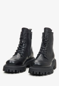 Black leather lace-up combat boots with thick rugged soles and side zippers, placed side by side on a white background.
