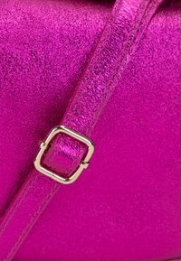 Metallic pink håndtaske med en tekstureret overflade, en matchende rem og en skinnende guldfarvet firkantet spænde detalje.