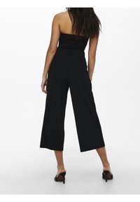 Pantalon noir à jambes larges avec une taille haute. Confectionné dans un tissu léger, présentant une texture lisse sans motifs apparents.