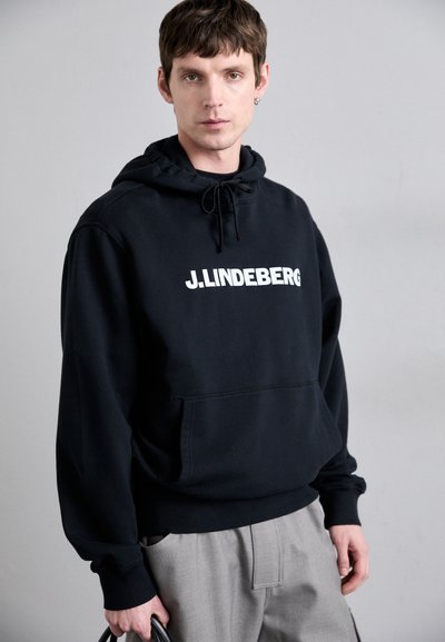 Felpa nera con cappuccio e cordoncino, caratterizzata da un grande logo bianco "J.LINDEBERG". Il materiale sembra morbido e liscio, con una tasca a marsupio.