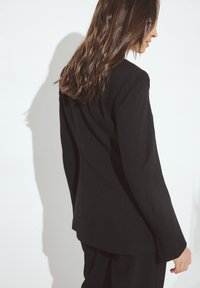 Zwarte getailleerde blazer met een strak ontwerp, lange mouwen en een soepele textuur. Beschikt over nette lijnen en een gestructureerde pasvorm, ideaal voor formele kleding.