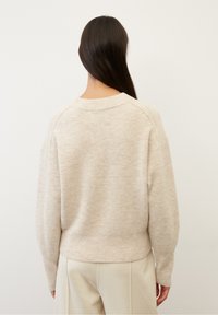 Jersey de punto beige con cuello redondeado, corte relajado y mangas raglán. La tela parece suave con una textura sutil y un dobladillo cropped.