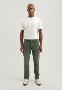 Pantalones de pana verde con corte recto, combinados con una camiseta ajustada blanca y zapatillas blancas. La tela tiene una textura suave.