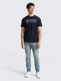 Camiseta de algodón azul marino con texto blanco impreso. Cuello redondo, mangas cortas, combinada con jeans de color azul claro y zapatillas blancas.