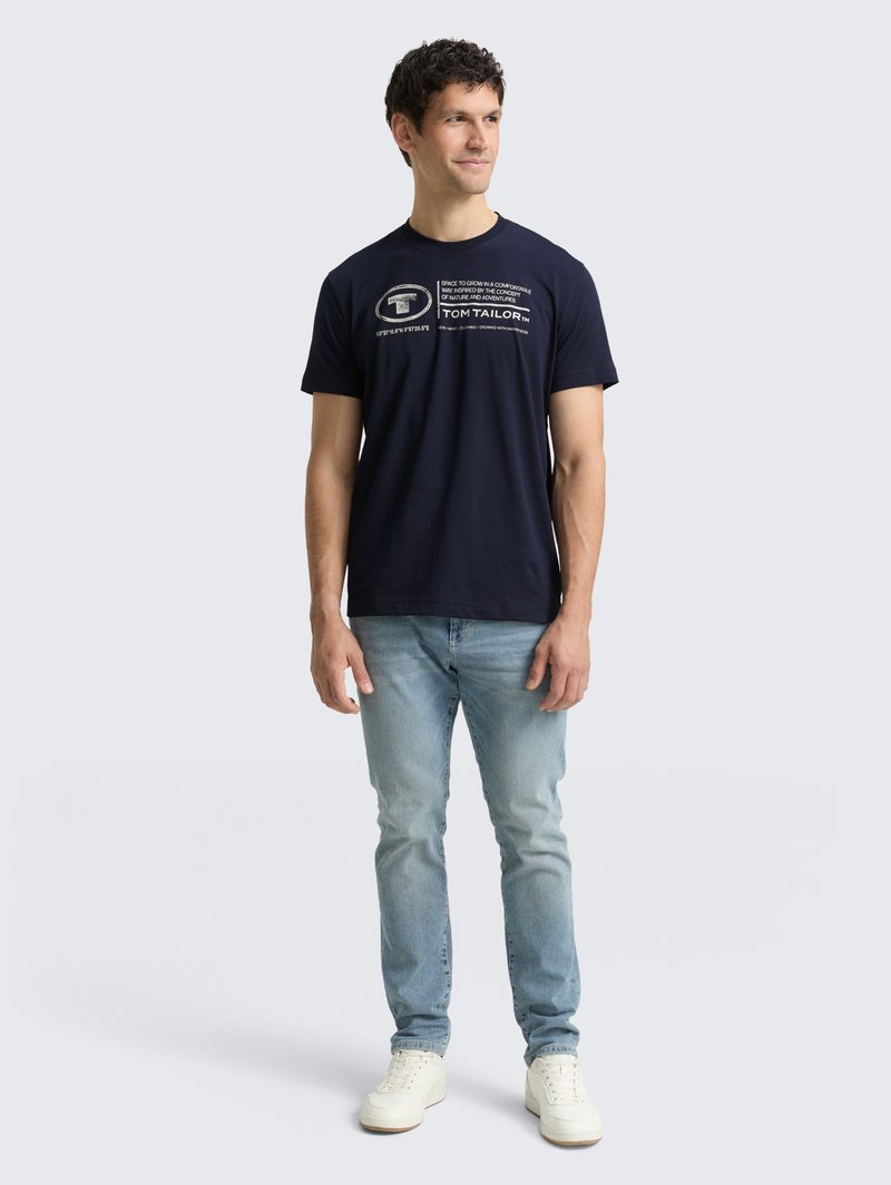 Granatowa koszulka bawełniana z nadrukowanym białym napisem. Okrągły dekolt, krótkie rękawy, zestawiona z jasnoniebieskimi dżinsami i białymi trampkami.