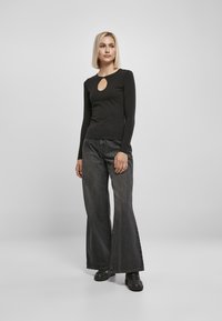 Sort langærmet top med nøglehulslukning, parret med brede mørke denim jeans og sorte sko. Simpel, tætsiddende design.