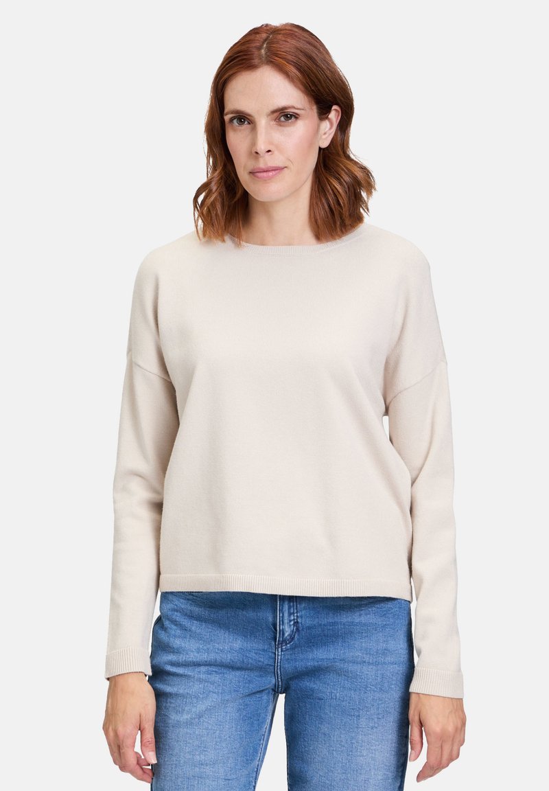 Pull beige clair, col rond, manches longues, bords côtes aux poignets et à l'ourlet, texture douce. Assorti avec un jean bleu. Design minimaliste.