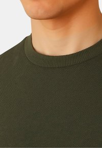 Maglione verde oliva in maglia con finitura strutturata, caratterizzato da una scollatura a girocollo a coste. Nessun motivo o dettaglio hardware visibile.