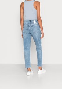 Ljust blå högmidjade jeans, rak benklippning, med två bakfickor och en vit logotyp. I kombination med vita sneakers.