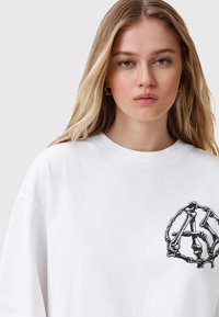 T-shirt in cotone bianco con scollo rotondo, caratterizzato da una grafica scheletrica nera nella zona a sinistra del petto. Vestibilità morbida.