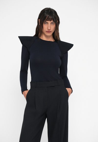 Blusa preta de mangas longas com ombreiras estruturadas, design ajustado e textura suave, combinada com calças de riscas verticais de cintura alta.