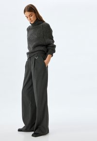 Grijze gebreide trui met een hoge hals en oversized mouwen, gecombineerd met donkergrijze, wijde broek met riemlussen en zijzakken.