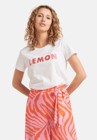 Witte katoen t-shirt met vetgedrukte roze tekst "LEMON", gecombineerd met roze broeken met een oranje zebra-streep patroon en een gestrikt middel.