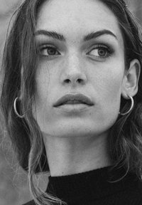 Ritratto in bianco e nero che ritrae una persona con capelli lunghi e orecchini a cerchio, su uno sfondo neutro. Il soggetto ha una pelle liscia e lineamenti ben definiti.