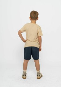 Beige bomull t-shirt, marinblå shorts, randiga strumpor, bruna sandaler; sedd bakifrån. Enkelt mönster, avslappnad passform, sömlös struktur.