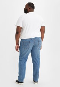 Jeans azul claro en un corte relajado con pierna recta. Cuenta con dos bolsillos traseros y una cintura de altura media. Combinados con una camiseta blanca.