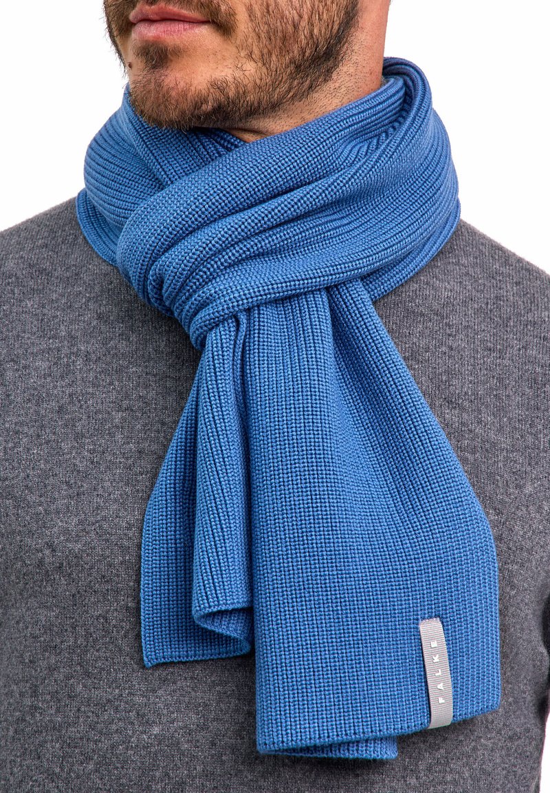 Sciarpa blu lavorata a maglia con una texture a coste, avvolta attorno al collo. Presenta un piccolo etichetta grigia con scritto "FALKE".
