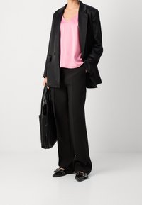 Woman wearing black blazer and pants with pink satin top, holding black textured tote bag, and black pointed shoes with buckles.