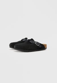 Fekete velúr slip-on klumpák állítható csat nélküli pántokkal és parafa talppal, egyszínű fehér háttéren.