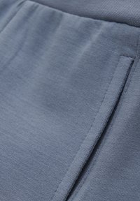 Helles blaues Gewebe mit einer weichen, strukturierten Oberfläche. Verfügt über ein Detail mit Seitentasche und einen glatten Bund.