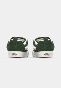 Zelene nubuk tenisice s bijelim detaljima, s potplatom za povlačenje i Vans logom na peti. Ravni gumeni potplat, zaobljen oblik.