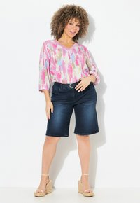 Värikäs monivärinen pusero V-päällä, kolmisen neljännestä hihoista; yhdistetty tummiin farkkushortseihin ja korkokenkiin. Suorat tekstit ja rento istuvuus.