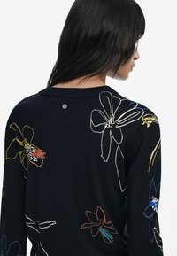Pull marin avec broderie florale multicolore, col rond et un petit logo au dos, texture de tissu lisse.
