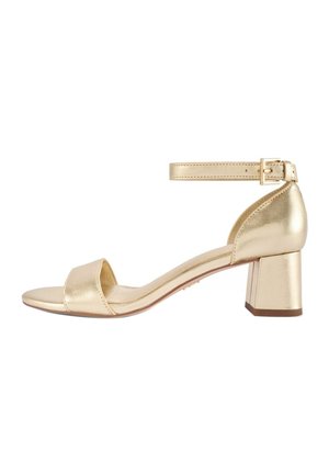 Złoty skórzany sandał na blokowym obcasie z odkrytymi palcami i regulowanym paskiem na kostkę z klamrą, pokazany z profilu na białym tle.