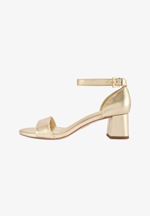 Złoty skórzany sandał na blokowym obcasie z odkrytymi palcami i regulowanym paskiem na kostkę z klamrą, pokazany z profilu na białym tle.