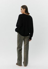 Melns pārāk liels džemperis un leopardu raksta brīvas formas bikses. Džemperim ir ribota mala, bet biksēm ir teksturēts dzīvnieku raksts brūnā un bežā krāsā.