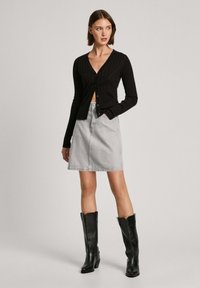 Svart ribbad cardigan med v-ringning och knappstängning, kombinerad med en ljusgrå denimkjol och knähöga svarta läderstövlar.