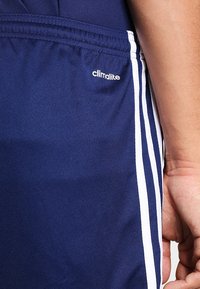 Shorts de sport bleu marine en tissu respirant avec des bandes blanches sur les côtés et un logo "climalite" près de la taille. Finition lisse et texturée.