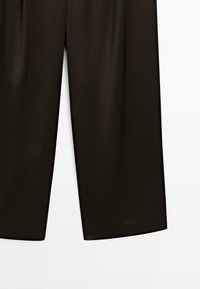 Black, flowy wide-leg trousers with smooth texture, featuring a high waist and subtle pleats, designed for a relaxed fit and a modern silhouette.