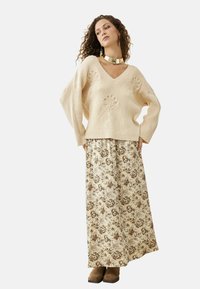 Suéter de punto color crema con escote en V y bordado floral, combinado con una falda larga estampada floral en tonos beige y marrón. Botines marrones.