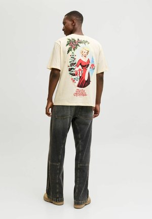 Beige bomulds T-shirt med en farverig vintage-inspireret grafik af en kvinde i en rød kjole, der holder gaver, prydet med juletema detaljer.