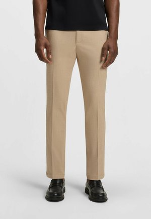 Beige tailored pants with a smooth texture and straight leg design, featuring a subtle weave pattern, paired with black loafers.