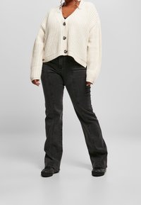 Krämmig stickad cardigan med V-hals och knappar, ihopparad med svarta utsvängda jeans med sidsömmar och enkla svarta skor.