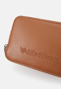 Brown leather wallet with embossed "VALENTINO" logo, featuring a zip closure and smooth texture. Rectangular shape with precise stitching.
