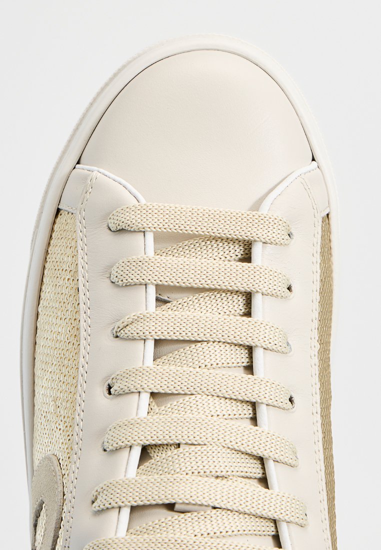 Zapatillas de cuero crema con paneles laterales de tejido trenzado, punta redonda y cordones planos. Presentan un diseño minimalista con texturas contrastantes.